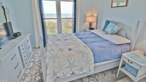 Un dormitorio con cama, mesita de noche, cómoda y ventana con vista al mar.