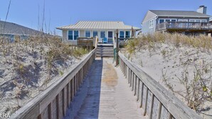 Una pasarela de madera que lleva a una casa de playa con porche y una escalera.