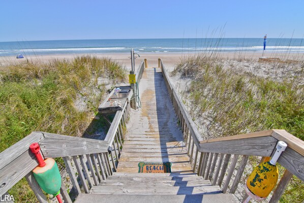 A wooden staircase leading to a beach with a sign reading "BEACH" and a lifeguard tower in the distance.