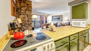 Una cucina con piano cottura, forno a microonde e pensili verdi. Si nota una parete in pietra e una finestra con vista sull'esterno.