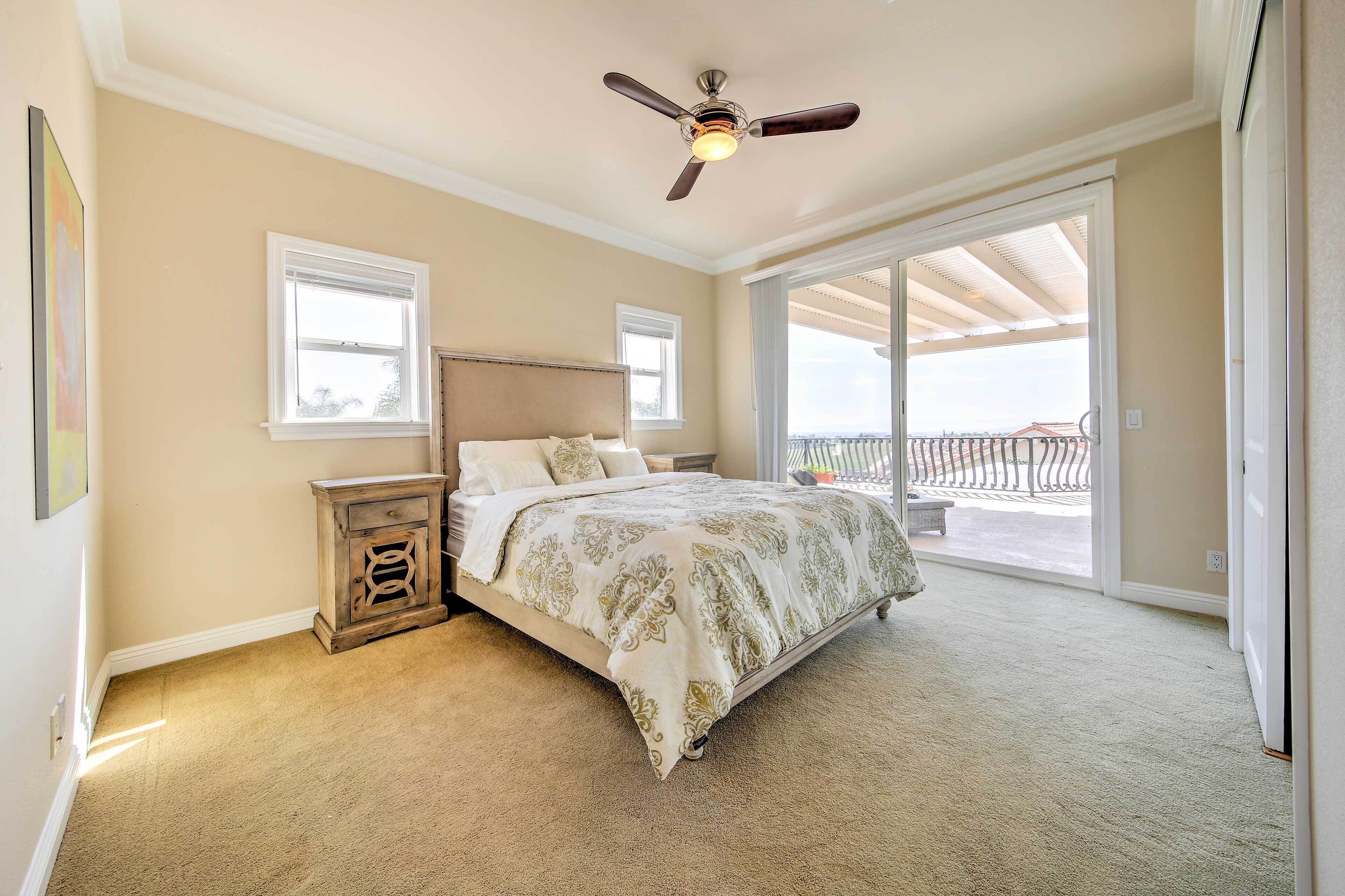 Une chambre à coucher comprenant un lit, une table de chevet, un ventilateur de plafond et une grande porte-fenêtre coulissante donnant sur un balcon.