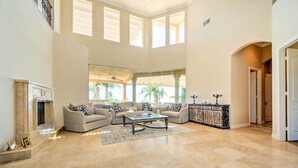 A spacious living room with a fireplace, two sofas, a coffee table, and a large window. - Luxe Wine Country Estate w/ Orchard-Facing Balcony (Temecula)