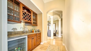 A kitchen with wooden cabinets, a wine rack, and a refrigerator. - Luxe Wine Country Estate w/ Orchard-Facing Balcony (Temecula)