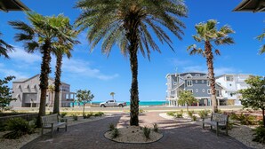 A paved walkway with benches, palm trees, and a building with a balcony overlooking the beach.