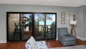 A living room with a view of the beach, a sliding glass door, a gray armchair, and a floor lamp.