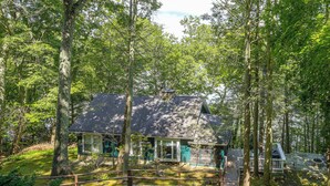A cabin surrounded by a forest with a wooden deck and a stone fireplace. - Dainty New Preston Cottage w/ Dock & Lake Views! (New Preston)
