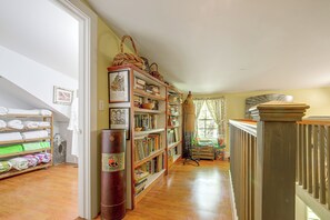Um corredor com piso de madeira, uma estante repleta de livros, um manequim e um radiador.