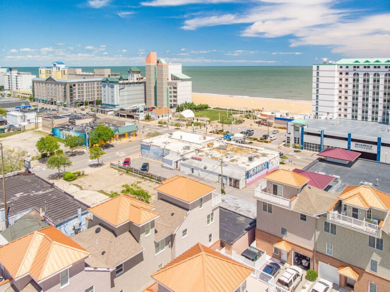 A coastal town with a mix of residential and commercial buildings, a beach in the background, and a clear sky.