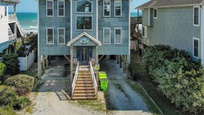 A two-story house with a front porch, a staircase leading to the entrance, and a view of the ocean.