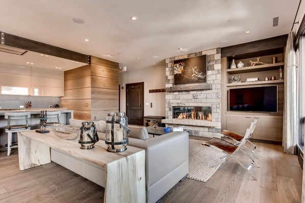A modern kitchen with a central island, a dining area with a sofa, and a fireplace with a mounted TV. - Luxurious Residence by InvitedHome | Ski-In/Ski-Out, Premier Kitchen, Modern (Edwards)