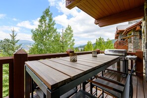 A wooden deck with a grill and outdoor seating area, overlooking a mountainous landscape. - Luxurious Residence by InvitedHome | Ski-In/Ski-Out, Premier Kitchen, Modern (Edwards)