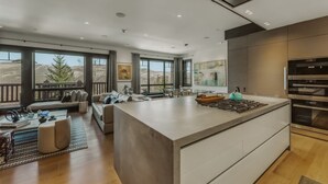 Een moderne keuken met een groot eiland, inbouwapparatuur en grote ramen met uitzicht op het buitengebied.