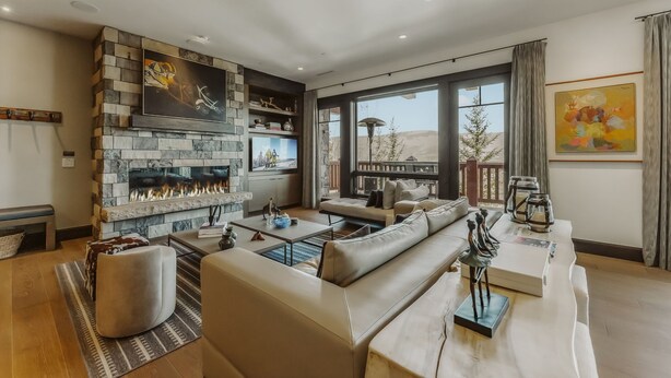 Een moderne woonkamer met een stenen openhaard, comfortabele zitplaatsen en grote ramen met uitzicht op de omgeving.