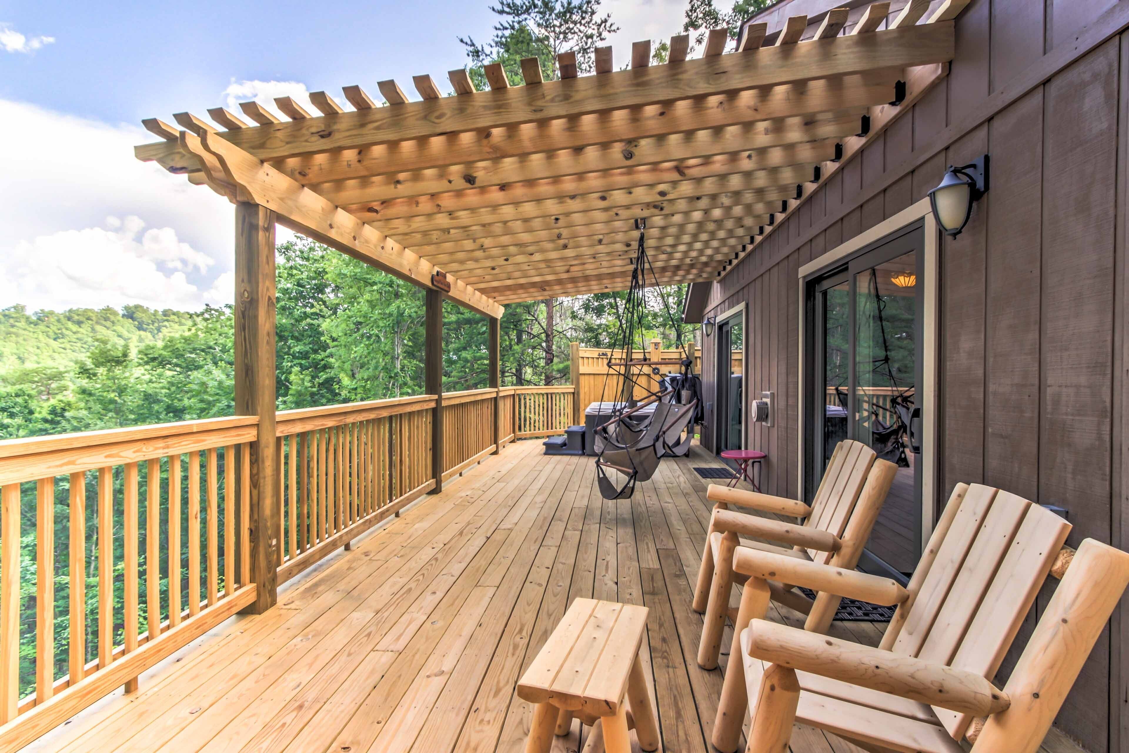 A wooden deck with a pergola, outdoor seating, and a hanging chair.