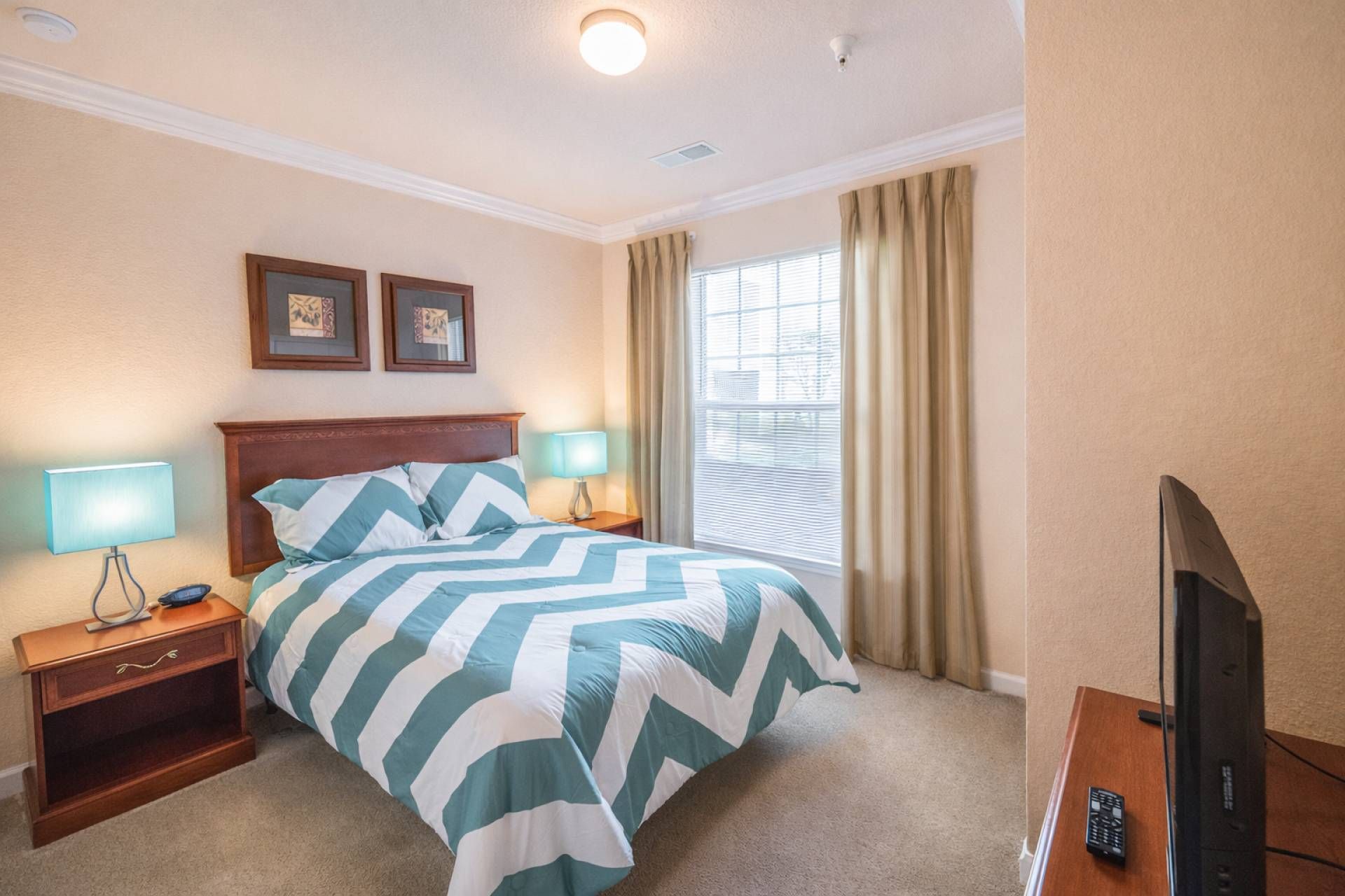 A hotel room with a bed, two bedside lamps, a television, and a window with curtains.