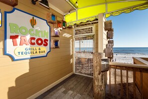 En restaurang som heter ”Rockin Tacos” med en skylt, en träveranda och utsikt över stranden.