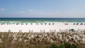 A beach with white sand, a wooden fence, and several beach umbrellas. - ETW 2005: Emerald Shore: Step Into Tranquility with a Beachfront Home! (Fort Walton Beach)