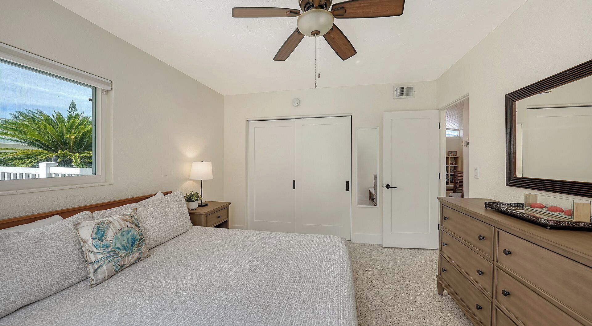 A bedroom with a bed, a nightstand, a dresser, a ceiling fan, and a closet.
