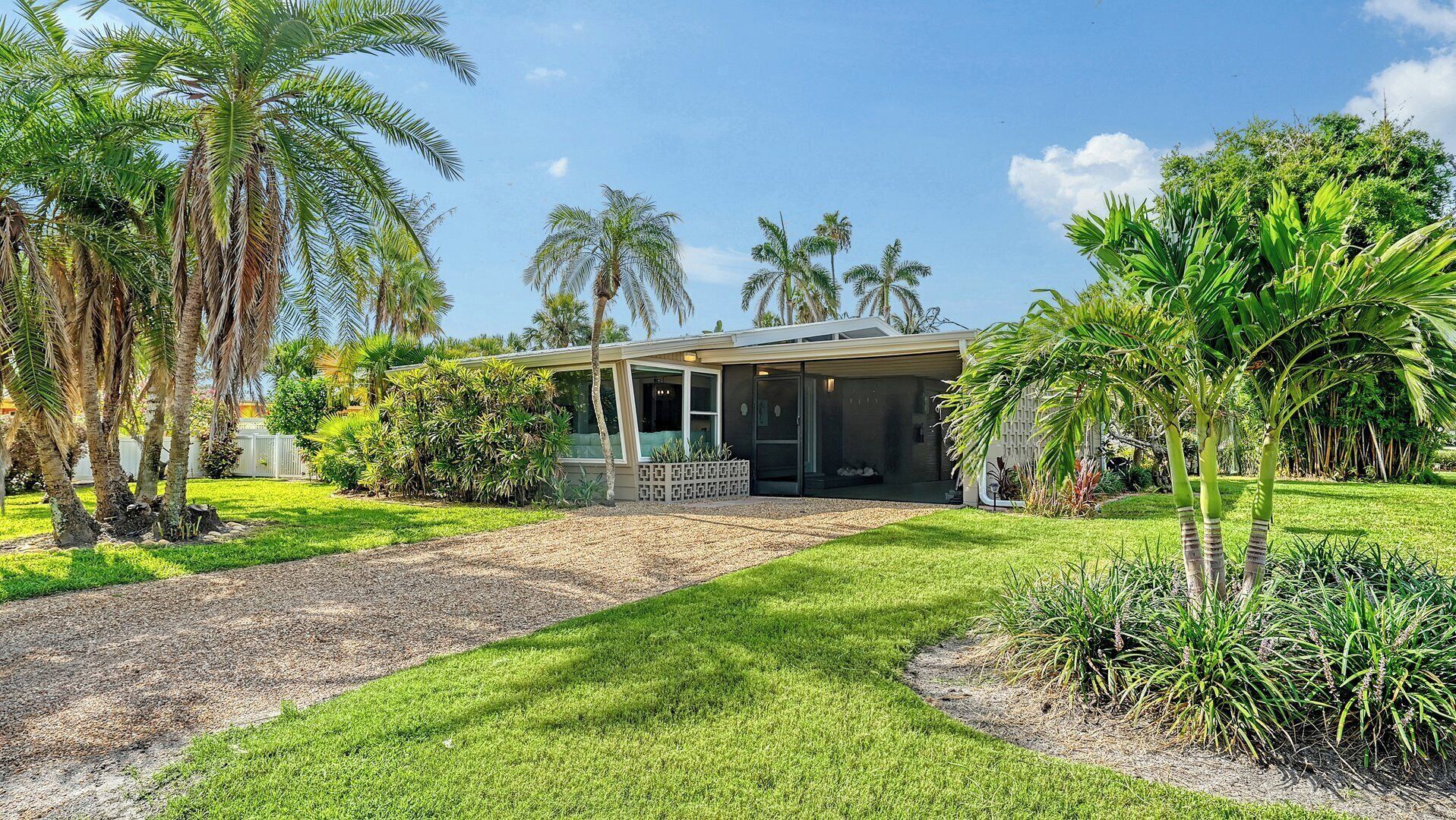 Une maison moderne dotée d’un patio couvert, entourée d’une végétation luxuriante et de palmiers.