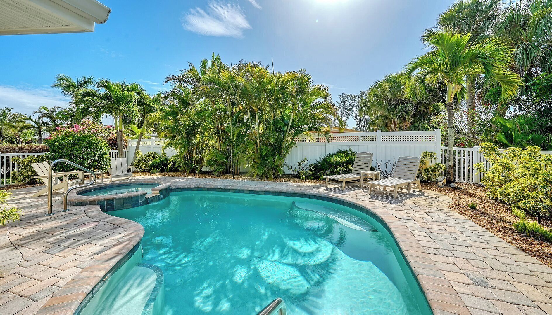 A swimming pool with a curved edge, surrounded by a patio area with brick flooring and white lounge chairs.