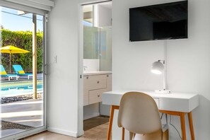 Una habitación con escritorio, silla, televisor y una puerta de vidrio que da a una zona de piscina al aire libre.