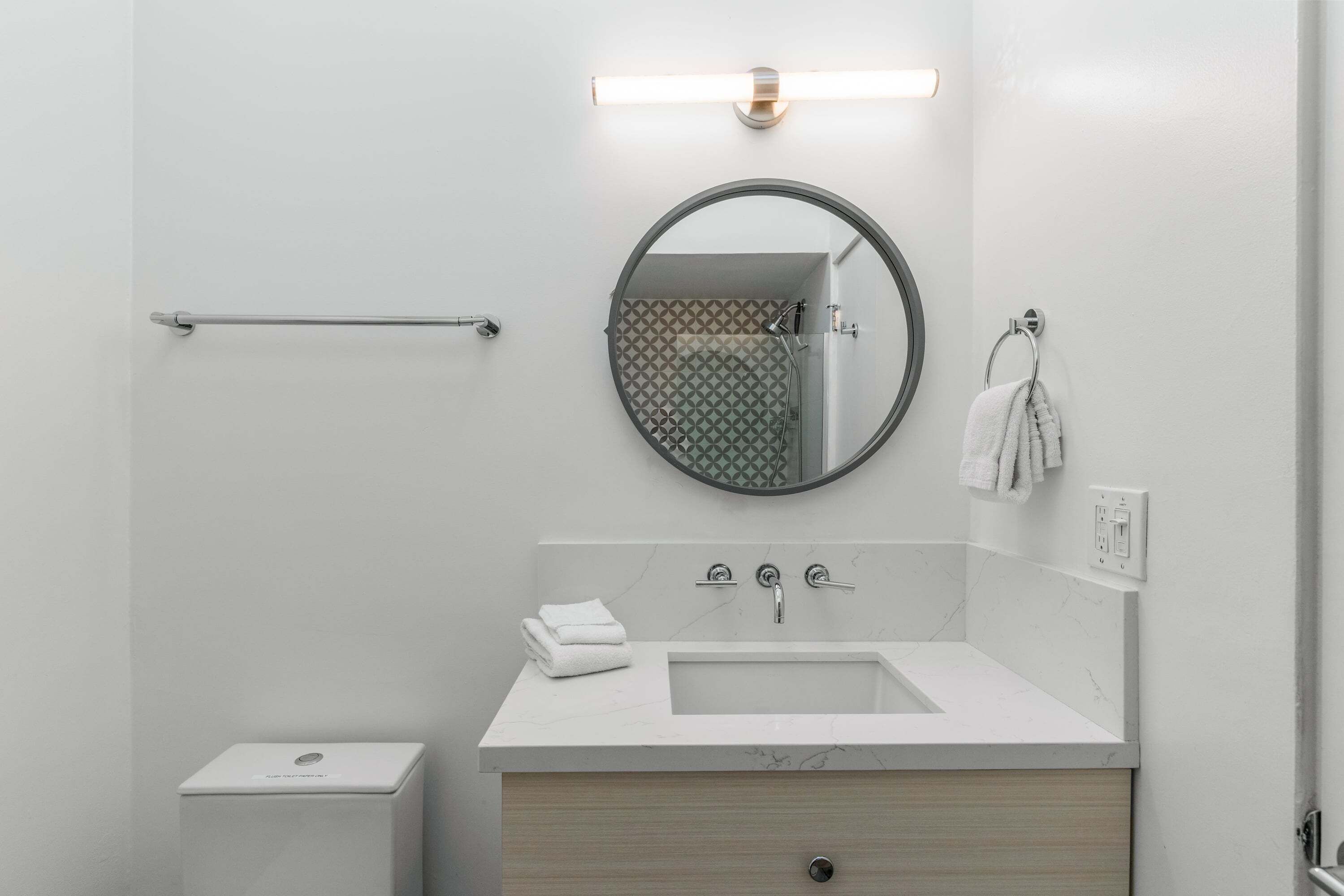 Um banheiro moderno com uma pia branca, um espelho redondo, um porta-toalhas e um vaso sanitário.