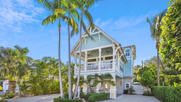 A two-story house with a balcony, surrounded by palm trees and a gravel driveway. - Beautiful Luxury Southern Style Home located in Anna Maria - Walk easily to Beach, Sleeps 6! (Anna Maria)
