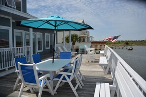 A wooden deck with a table and chairs, an umbrella, and a view of the water.