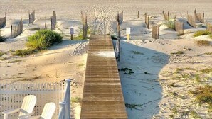 Et træbroareal der fører til en strand, med et hegn og stole.