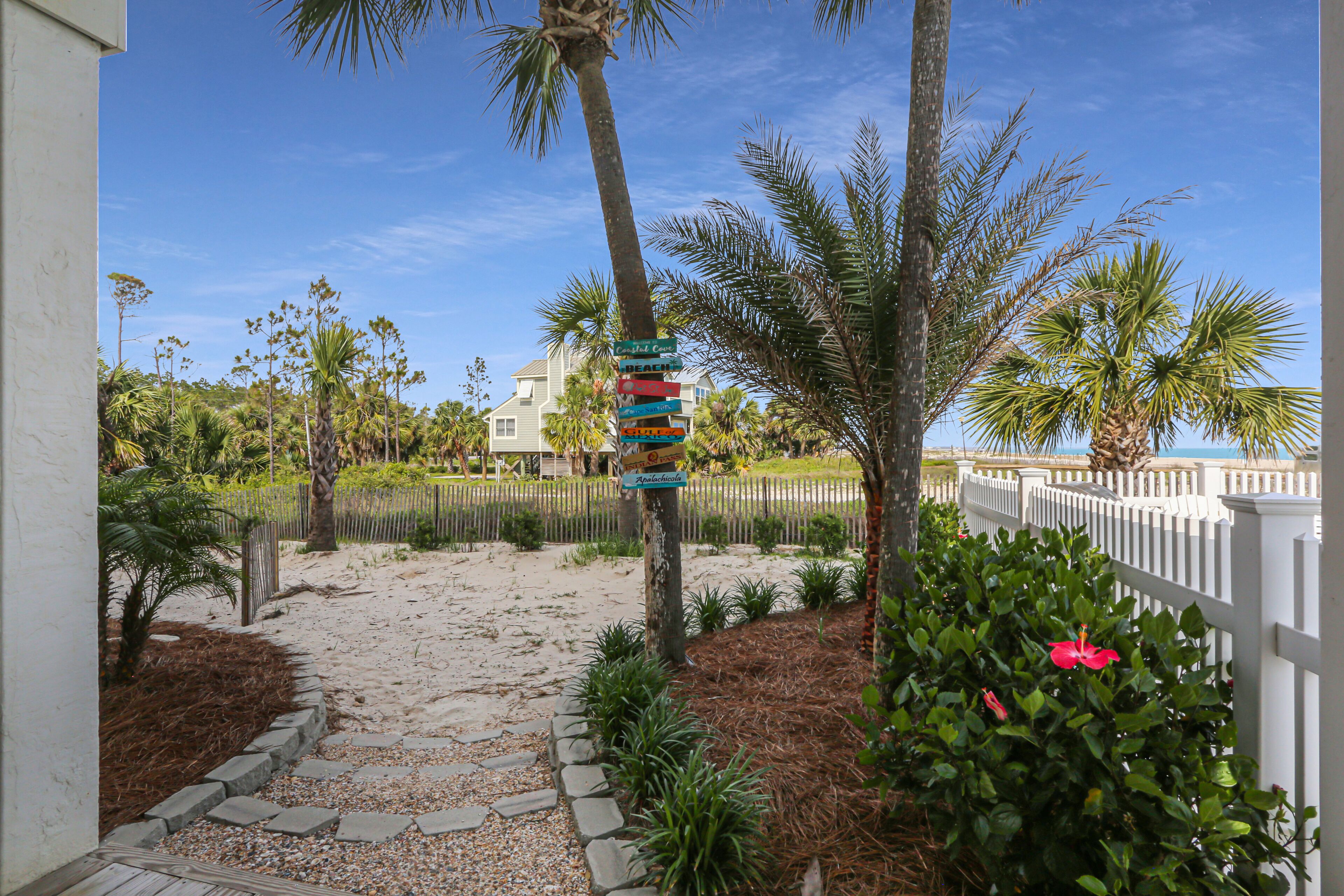A pathway leading to a house with a white fence and palm trees.
