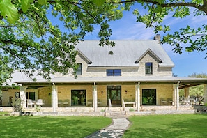 A two-story stone house with a covered porch, a stone staircase, and a lawn. - Rio De Los Suenos is the perfect hill country destination in every season. (Wimberley)