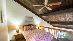 A bedroom with a bed, two bedside lamps, a ceiling fan, a wooden headboard, a framed picture on the wall, and a balcony with a chair. - Hale Kamaole 340  Third floor condo, easy access to best beach on Maui! (Kihei)
