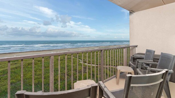 A balcony with a view of the ocean, outdoor furniture, and a grassy area.