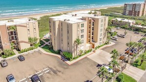 A multi-story hotel with a parking lot and a view of the beach.