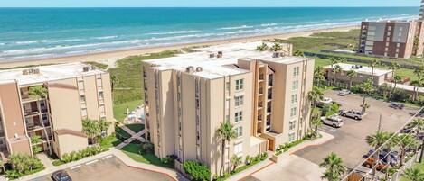 A multi-story hotel with a parking lot and a view of the beach.