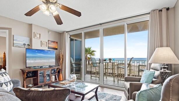 A living room with a TV, a ceiling fan, and a view of the beach. - IP 213: Starlight Retreat - Kick back, relax, and enjoy Gulf-Front Living! (Fort Walton Beach)