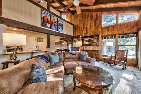 A spacious living room with a large sectional sofa, a glass coffee table, and a wooden ceiling with exposed beams.