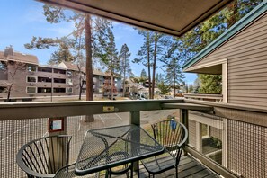A balcony with a metal table and chairs, overlooking a residential area with houses and tall trees.