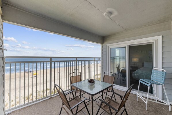 A balcony with a table and chairs, overlooking a beach.