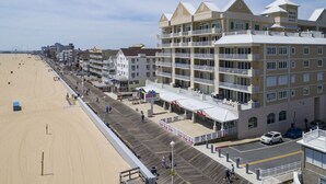 Een hotel aan het strand met meerdere balkons, een houten looppad en een zandstrand.