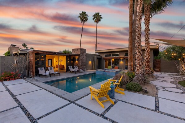 A modern outdoor pool area with a stone patio, lounge chairs, and palm trees.
