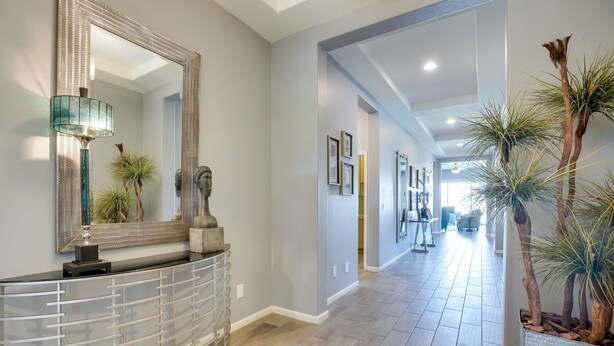 A hallway with a glass partition, a mirror, a lamp, and potted plants.