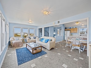 A spacious living room with a sofa, coffee table, and dining area with chairs. - Sounds Like Fun - Relax Soundside with Your Pet! (North Topsail Beach)