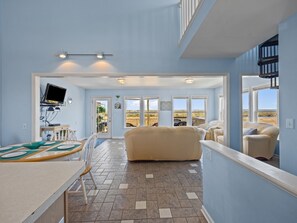 A spacious living area with a large sofa, a dining table with chairs, and a TV mounted on the wall.