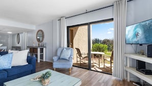 A modern living room with a blue sofa, a striped armchair, a coffee table, and a TV on a stand. - Beachfront Walkout – Ground-Floor Oceanfront Retreat w/ Private Sand Access & Heated Pool (Cape Canaveral)