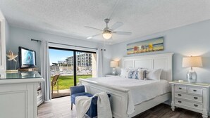 A bedroom with a large bed, a desk with a TV, a ceiling fan, and a view of the outside. - Beachfront Walkout – Ground-Floor Oceanfront Retreat w/ Private Sand Access & Heated Pool (Cape Canaveral)