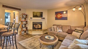 A living room with a fireplace, a dining area with chairs, a sofa with cushions, and a coffee table. - Walk to Lifts: Main Street Breck Condo w/ Mtn View (Breckenridge)
