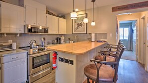 A modern kitchen with stainless steel appliances, a wooden island with bar stools, and a fire extinguisher mounted on the wall. - Walk to Lifts: Main Street Breck Condo w/ Mtn View (Breckenridge)