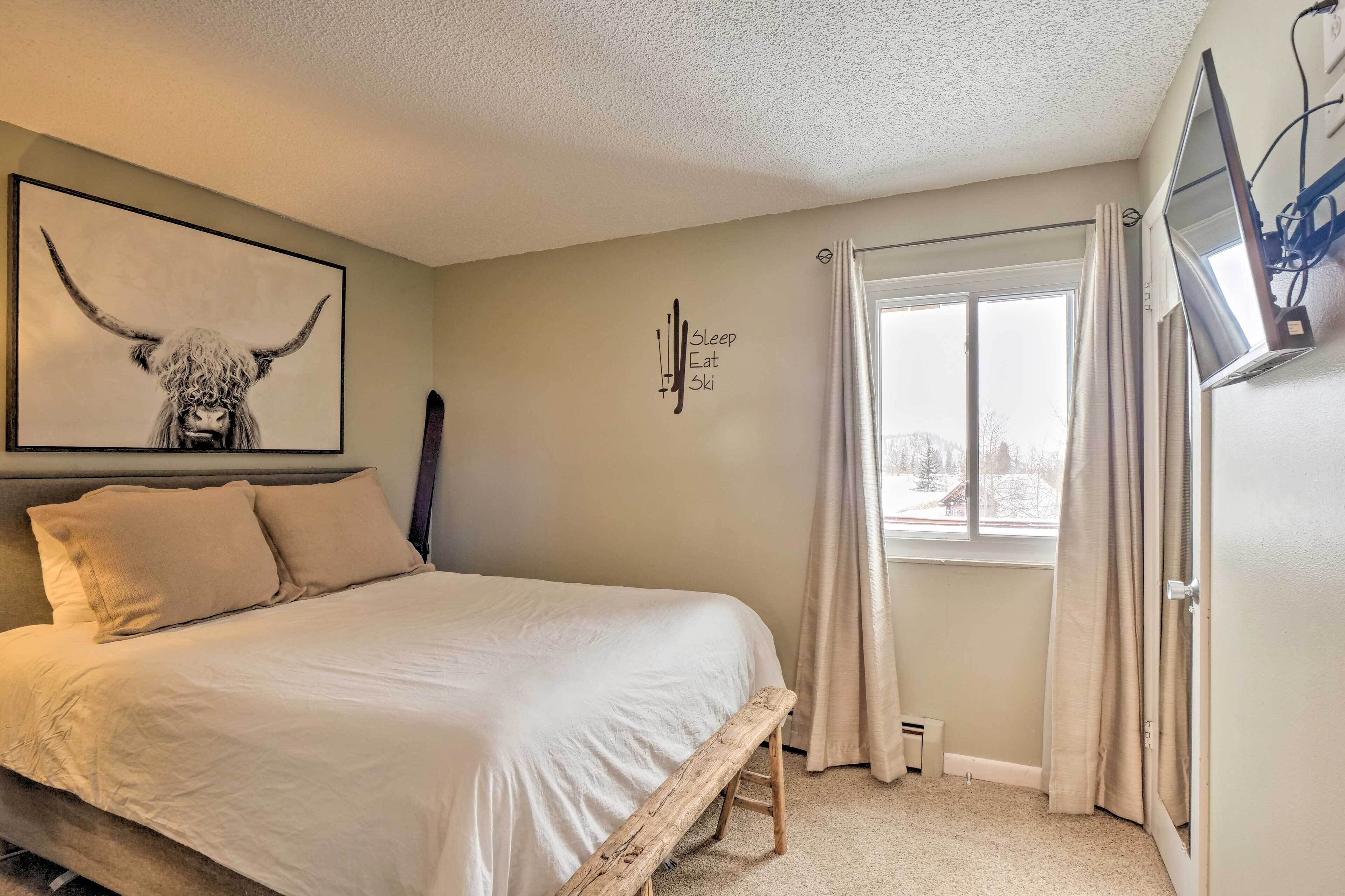 A bedroom with a bed, a mounted TV, a window with curtains, and a wall art of a bull.