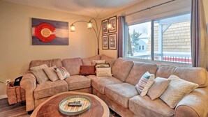 A living room with a sectional sofa, a coffee table, and a large window with a view of a building outside. - Walk to Lifts: Main Street Breck Condo w/ Mtn View (Breckenridge)